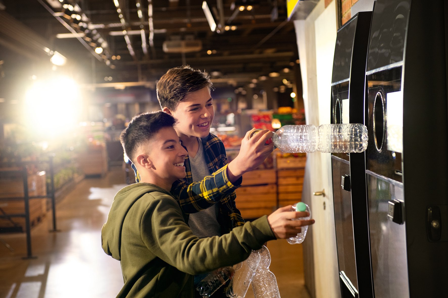 two boys putting bottles into a reverse vending machine